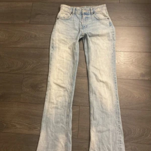 Ljusblå bootcut jeans från ZARA - Säljer ett par ljusblå bootcut jeans från ZARA med klassisk femficksdesign och råa kanter nertill. Jeansen är tillverkade i denim med en lätt tvättad look. Perfekta för dig som gillar en avslappnad men trendig stil. Dom år middwaist och långa 