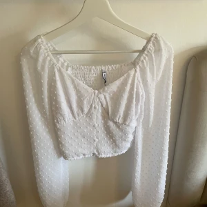 Vit blus med prickig struktur från New Yorker - Säljer en söt vit blus från New Yorker i storlek XXS. Resår i ryggen för skön passform och lätt croppad modell. Använd enstaka gånger, fint skick. Mer än XS skulle jag säga.