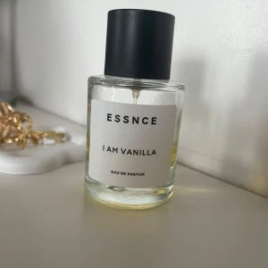 ESSNCE I Am Vanilla Eau de Parfum - En stilren parfymflaska med svart lock och transparent glas, fylld med en gyllengul vätska. Doften heter I Am Vanilla och är en Eau de Parfum från ESSNCE. Flaskan har en  minimalistisk vit etikett med svart text. Se hur mycket som är kvar på bilden