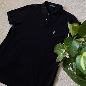 Polo Ralph Lauren Black Polo T-Shirt - Classic Polo Ralph Lauren short-sleeve polo shirt in black, men’s size M. Timeless and versatile, made from high-quality cotton with the signature embroidered pony logo in white. The shirt is in excellent condition with no stains, tears, or fading – gently worn and well taken care of.  Perfect for both casual and smart outfits. 100% authentic. Fast shipping and open to reasonable offers.