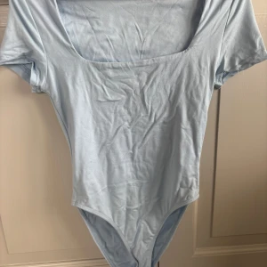 Ljusblå body med kort ärm - Säljer en ljusblå bodysuit med rundad urringning och korta ärmar. Perfekt att styla med jeans eller kjol för en enkel och fräsch look. Mjuk och stretchig känsla.