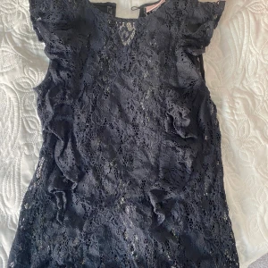 Superfin svart spetsblus med volanger💓🌼 - Säljer en svart blus i spets med volangdetaljer längs sidorna. Blusen har korta ärmar och ett fint hålmönster i spetsen. Perfekt att styla med jeans eller kjol för en snygg look.
