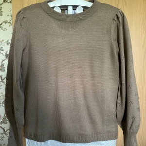 Beige stickad tröja med puffärmar från Vila - Säljer en beige stickad tröja från Vila med fina puffärmar och diskreta hålmönster på ärmarna. Tröjan har rund halsringning och långa ärmar, oanvänd. 