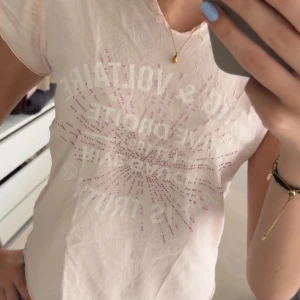 Ljusrosa t-shirt med tryck från Zadig & Voltaire - Säljer en ljusrosa t-shirt från Zadig & Voltaire med glittrigt tryck framtill. Använd ganska mycket men i bra skick, ganska många stenar har ramlat av men inget man tänker på