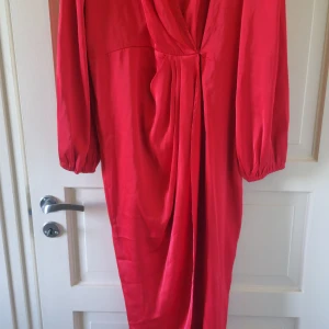 Röd omlottklänning från SHEIN - Säljer en röd omlottklänning från SHEIN i storlek XL. Klänningen har långa ärmar med lätt puff och v-ringad omlottdesign framtill. Perfekt för dig som vill ha en färgstark och elegant look.