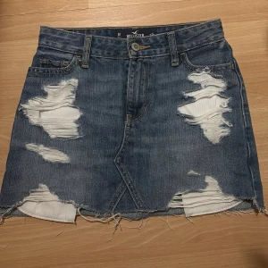 Blå jeanskjol från Hollister - Säljer en blå jeanskjol från Hollister med slitna detaljer och rå kant nertill. Kjolen har klassisk femficksdesign och är i en kort modell. Perfekt för dig som gillar en avslappnad och trendig stil. säljer då den är för liten för mig. kontakt för fler foton eller liknande💘💘 använd 1 gång 💘