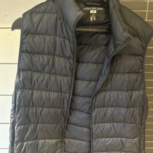 Svart dunväst från Uniqlo Ultra Light Down - Säljer en svart, lätt och smidig dunväst från Uniqlo Ultra Light Down. Västen har en hög krage och är quiltad med horisontella sömmar. Perfekt att bära som lager under jackan eller över en hoodie. Finns ett litet hål i västen som man inte märker av
