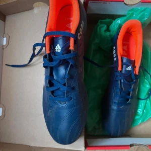 Adidas Copa fotbollsskor blå och orange - Säljer ett par Adidas Copa fotbollsskor i blått med orange insida och vita detaljer. Skorna har snörning och är designade för fotboll. Klassisk rund tå och platt sula för bra grepp på planen.
