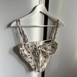 Blommig korsettopp  - Supersöt korsettopp med blommigt mönster i blått och gult på en beige bakgrund.