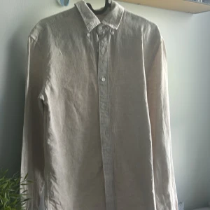 Beige linneskjorta med knappar - Snygg beige skjorta i 100% linne från C. Skjortan har klassisk krage, långa ärmar och knäppning framtill. Perfekt för en stilren och luftig look under varmare dagar.