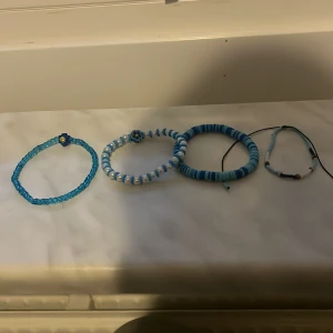 Fyra blå armband med pärlor - Säljer fyra olika armband i blå toner. Två av armbanden har små pärlor, ett har större platta pärlor och ett har en mix av blå och vita pärlor. Perfekta för att ge en färgklick till din stil!