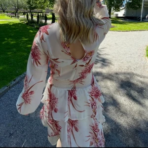 Vit blommig klänning från Gina Tricot - Säljer en söt vit klänning från Gina Tricot med rosa blommönster. Klänningen har lång ärm, markerad midja och volangdetaljer på kjolen. Perfekt för vår och sommar, superfin till ljusa dagar!