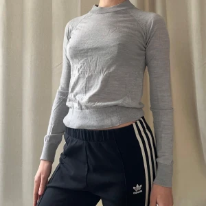 Ljusgrå polotröja från Stockh LM - Säljer en ljusgrå, tunn och mjuk polotröja från Stockh LM. Tröjan har lång ärm, ribbade muddar och hög hals. Perfekt att styla med jeans eller kjol för en enkel och stilren look.