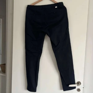 Mörkblå chinos från Mouli - Säljer ett par mörkblå chinos från Mouli i storlek w31. Byxorna har normal passform, knäppning med knapp och dragkedja samt två bakfickor med knappar. Perfekta för en stilren och avslappnad look.