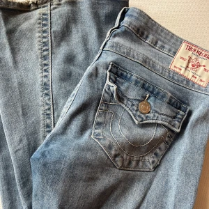 Ljusblå jeans Joey Low Rise Flare från True Religion - Säljer ett par ljusblå jeans från True Religion, modell Joey Low Rise Flare. Jeansen har låg midja, utsvängda ben och dekorativa sömmar samt ficklock bak. Klassisk knappstängning och slitna detaljer vid benslut.