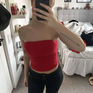 Röd tubtopp -  röd tubtopp med lätt rynkad effekt. Toppen är axelbandslös och sitter tight mot kroppen. Perfekt för dig som vill ha en enkel men snygg topp till sommaren. Superfint skick! 