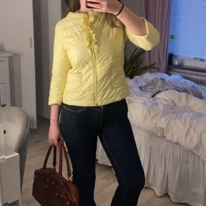 Trekvartsärmad jacka - Ljusgul quiltad jacka med dragkedja framtill och diskret volangdetalj vid dragkedjan. Jackan har trekvartsärm och två fickor framtill. Perfekt för vår eller sommar och ger en fräsch look till din outfit. Finns en liten defekt som man kan se på sista bilden.