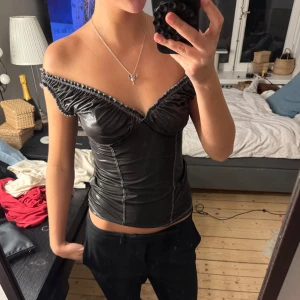 Svart offshoulder topp - Säljer en svart offshoulder topp med markerade sömmar och lätt glansigt material. Passar s/xs