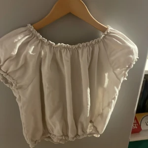 Vit offshoulder blus - Säljer en söt vit offshoulder blus med resår vid halsringning och midja. Blusen har korta puffärmar och är gjord i ett lätt, luftigt tyg. Perfekt för varma dagar och enkel att styla med olika outfits.