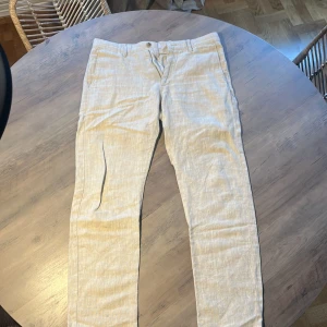 Beige linnebyxor från NN07 - Snygga och stilrena beige linnebyxor från NN07. Byxorna har normal passform, klassisk midja och stängs med dragkedja och knapp. Perfekta för varmare dagar tack vare det svala linnematerialet. Nypris 1799kr! Mitt pris endast 299kr🙌🎉