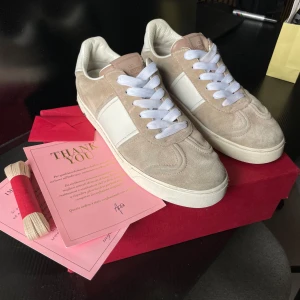 Beigea valentino flycrews - Snygga sneakers i beige mocka med vita skinnpaneler och vita skosnören. Skorna har rund tå, platt sula och små silverfärgade nitar på hälen. Perfekta för dig som gillar stilrena och exklusiva sneakers👊 Jag har bytt snörena men man får såklart med orginal snörena och ett par extra💯mockan är lite missfärgad på sina ställen men inget som man tänker på! 3 nitar är av på skon tyvärr men går att köpa till på andra ställen :) hör av er vid minsta lilla fundering⭐️