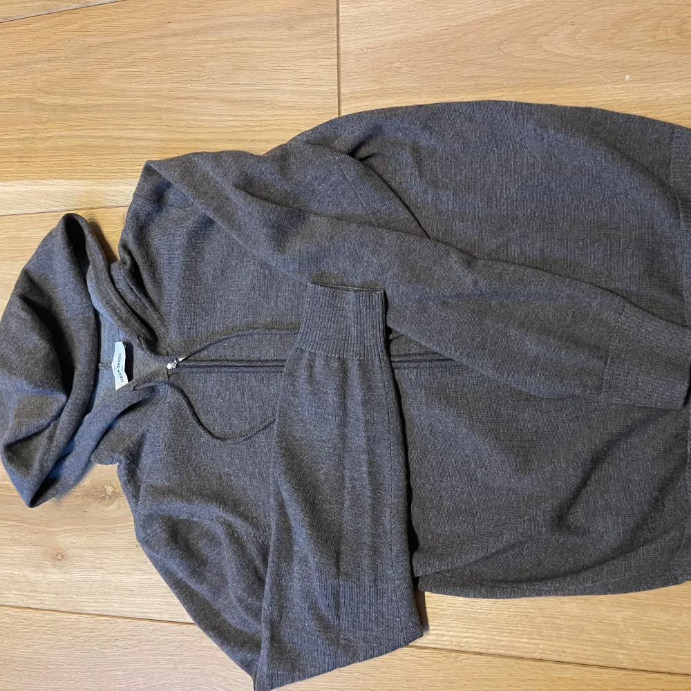 Mysig mörkgrå hoodie från Gran Sasso med dragkedja framtill och huva. Perfekt för lager-på-lager och chill dagar. Ribbad mudd vid ärmslut och nederkant. Enkel och stilren design.. Hupparit & Collegepaidat.