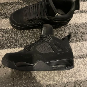 Nike Air Jordan 4 black cat - Säljer ett par helsvarta Nike Air Jordan 4 med klassisk siluett och Jumpman-logga på plösen. 