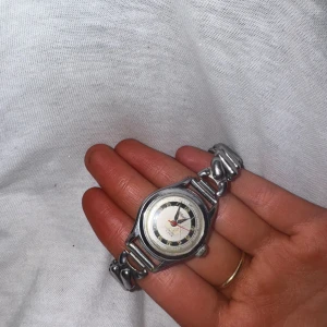 Silverfärgad armbandsklocka med metallarmband - Säljer en stilren armbandsklocka i silverfärgad metall. Klockan har ett runt ur med svart och vit urtavla samt ett klassiskt länkarmband. Perfekt accessoar för dig som gillar tidlös design.