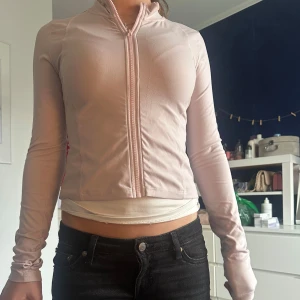 Ljusrosa tränings jacka med dragkedja - Säljer en ljusrosa, tränings jacka med dragkedja framtill. Jackan har lång ärm och en tight passform som framhäver figuren. Perfekt för dig som gillar en sportig och stilren look.
