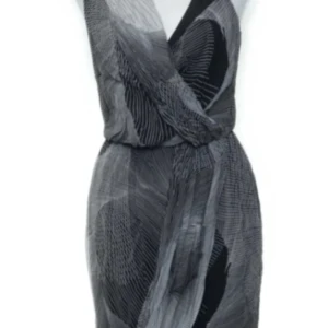 Warehouse klänning i silke - Säljer en ärmlös klänning i svart och grått med abstrakt mönster. Klänningen har omlott-effekt upptill och är tillverkad i 100% silke med polyester-detaljer och viskosfoder. Perfekt för dig som gillar unika mönster och sköna material.