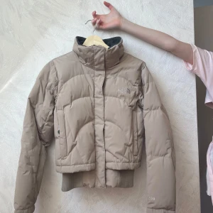 North Face jacka - Säljer en beige pufferjacka från The North Face med hög krage och ribbade muddar. Jackan är en kortare modell och åtsittande längst ner. Riktigt snygg och trendig!🤩Står ej storlek, uppskattar kring S.