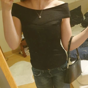 Svart offshoulder topp från H&M - Säljer en svart ribbad offshoulder topp från H&M. Toppen har en snygg, åtsittande passform och bred krage som vilar över axlarna. Perfekt för dig som gillar stilrena och trendiga plagg. Suuupersnygg och elegant! Liten passform.