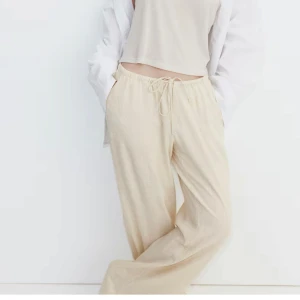 Beiga vida linnebyxor med dragsko - Säljer ett par beiga linnebyxor med avslappnad passform och dragsko i midjan. Byxorna har raka, vida ben och är perfekta för en chill och stilren look. Lätta och luftiga, passar perfekt till varmare dagar.