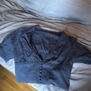 Mörkblå blus med knappar och spetsdetaljer - Säljer en mörkblå blus med v-ringning, spetsdetaljer   Blusen e lite kortare i modellen 