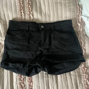 Svarta jeansshorts - Svarta jeansshorts med klassisk femficksdesign och uppvikta benslut. Gjorda i stretchigt material för extra komfort. Perfekta för varma dagar och enkel att matcha med olika toppar.