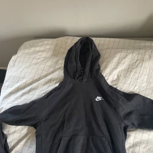 Svart hoodie från Nike - Säljer en svart hoodie från Nike med klassisk logga på bröstet. Tröjan har huva med dragsko och en stor magficka framtill. Perfekt för en avslappnad stil. Storleken är i barnstorlek och är M