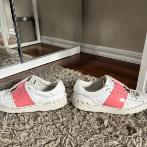 Valentino garavani  open sneakers - Säljer ett par vita Valentino garavani sneakers med en bred, glansig rosa rem över mitten. Storlek 38 men skulle säga att de även passar 38,5-39. Hör av dig för fler bilder🌺