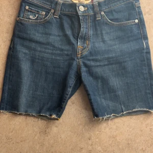 Blå jeansshorts från Jacob Cohen - Säljer ett par snygga shorts från Jacob Cohën i storlek 28. Modellen har en något slitad look nertill – vilket är en del av designen – och de har använts men är i fint skick utan några större defekter. Perfekta för sommaren om du gillar en avslappnad men stilren stil.  Skicka gärna ett meddelande vid frågor eller om du vill ha fler bilder! 