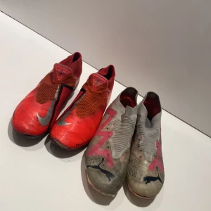 Gråa och röda  fotbollsskor från Puma och Nike  - Säljer två par skor ett par grå och ett par röda. De gråa fotbollsskorna är  från Puma och har rosa detaljer. Skorna har svarta Puma-loggor på sidorna och en strumpliknande passform för extra komfort på planen. De röda skorna är signerade av Ken zema som är en landslagsspelare och som spelat i watford. De röda är stl 41 och de rosa vita är stl 41 också. 200 för båda.