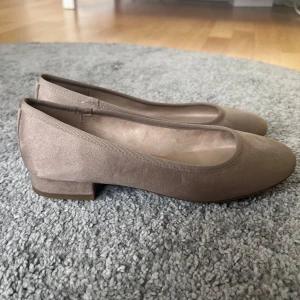 Beige ballerinaskor från Graceland - Säljer ett par stilrena beige ballerinaskor från Graceland med låg klack och rund tå. Skorna har en klassisk design och är tillverkade i syntetmaterial med mjuk finish. Perfekta för dig som gillar enkel och tidlös stil.