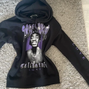Svart hoodie med 2PAC-tryck - Svart jätte mjuk o skön hoodie med stor bild på 2PAC och lila detaljer. Texten 'California Love' syns både på framsidan och längs ena ärmen. Mjuk insida och huva. Köpte den på carlings för typ 700 och den är endast använd 1 gång så är helt som ny! Den är i storlek xs.