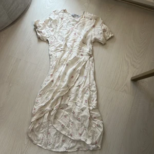 Blommig omlottklänning från 157 - Söt ljus omlottklänning från 157 med blommigt mönster i rosa och grönt. Klänningen har korta ärmar, v-ringning och resår i midjan. Perfekt för sommarens alla tillfällen!