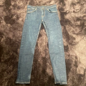 Blå slim fit jeans från J.Lindeberg - Säljer ett par klassiska blå jeans från J.Lindeberg i modellen Jay. Jeansen har slim fit passform, normal midja och fem fickor. Snygga kontrastsömmar och stilren design, perfekta till många olika outfits.