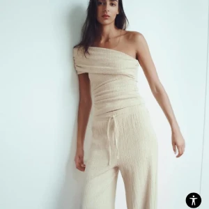 SÖKER Beige oneshoulder topp - Säljer en snygg beige topp med oneshoulder-design och smal passform. Toppen har en ribbad struktur och är perfekt för dig som vill ha en trendig och stilren look.