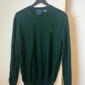Mörkgrön tröja från Polo Ralph Lauren - Säljer en mörkgrön långärmad tröja från Polo Ralph Lauren med rund halsringning och diskret broderad logga på bröstet. Klassisk och stilren modell som passar perfekt till många olika outfits.