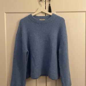 Ljusblå stickad tröja från Gina Tricot - Supermysig ljusblå stickad tröja från Gina Tricot i storlek XS. Tröjan har rund halsringning, långa ärmar och breda ribbade muddar vid ärmslut och nederkant. Perfekt för kyliga dagar och enkel att matcha med jeans eller kjol.