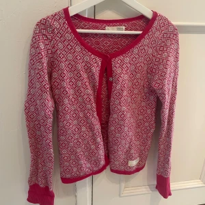 Rosa mönstrad kofta från Odd Molly - Superfin rosa kofta från Odd Molly med vitt geometriskt mönster och ribbade muddar. Koftan har långa ärmar och knäppning framtill. Kommer med en extra knapp. Modell 999M-746