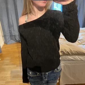 Svart stickad offshoulder-tröja - Säljer en svart stickad tröja med offshoulder-design. Tröjan har lång ärm och är ribbad i materialet vilket ger en snygg struktur. Perfekt för dig som vill ha en stilren men ändå trendig look.