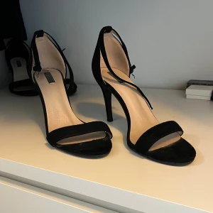 Svarta klackskor från Nelly - Säljer ett par svarta klackskor från Nelly med smal rem över tårna och justerbart spänne vid ankeln. Skorna har hög klack och öppen tå. Använda ett ytterst fåtal gånger. Skicka gärna prisförslag om du är intresserad🖤