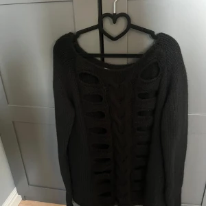 Svart stickad tröja med håldetaljer - Svart stickad tröja med unika håldetaljer och flätmönster framtill. Tröjan har rund halsringning och långa ärmar. Perfekt för dig som vill ha en stickad tröja med lite edge.